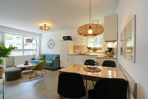 Ein modernes Wohnzimmer mit Sofa, Couchtisch und Esstisch. Es gibt eine Küchenzeile mit Spüle und Schränken.