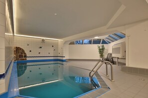 Una piscina interior con borde de azulejos azules, pared de piedra y un banco.