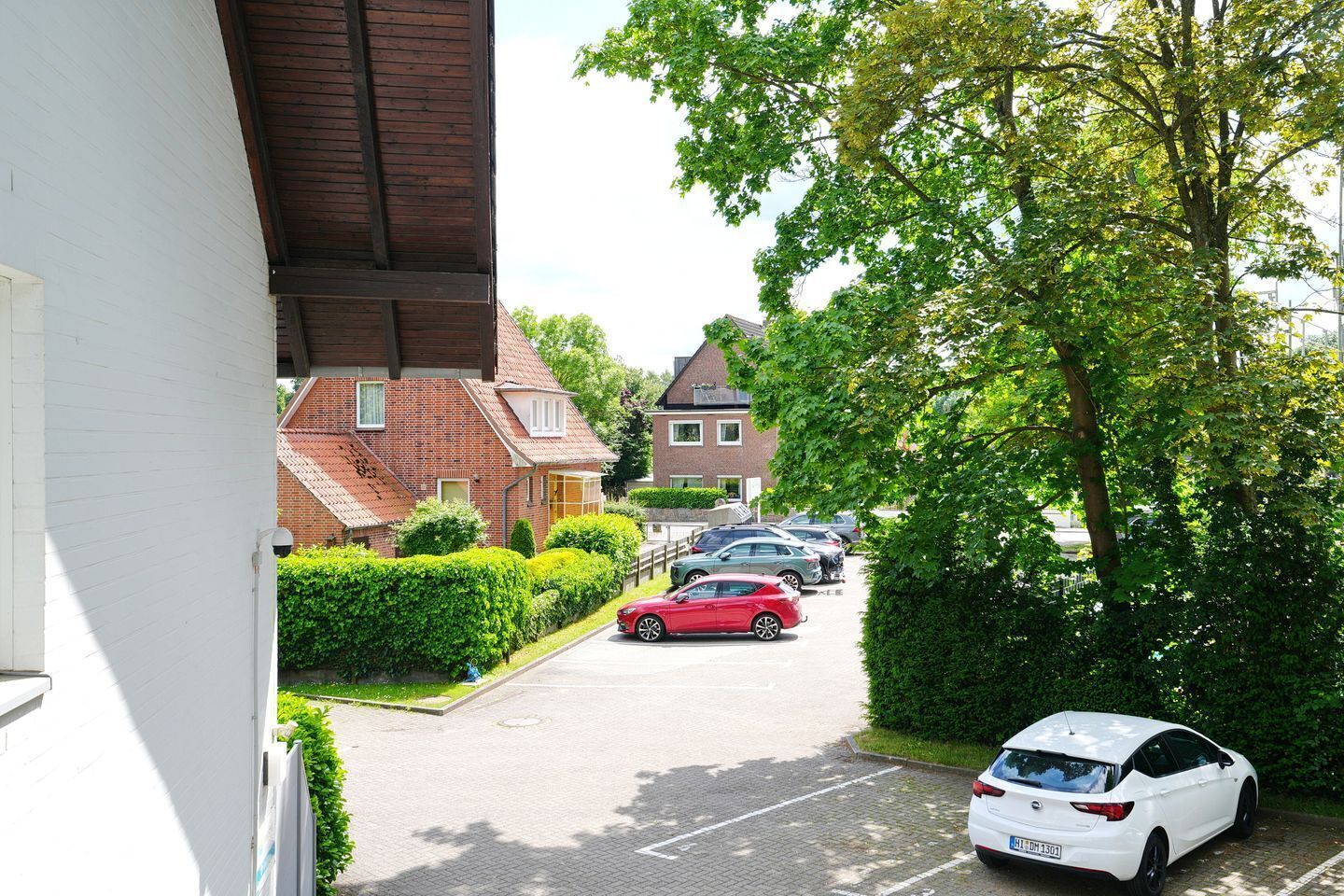 A residential street with parked cars, a red car in the foreground, and a white car in the background.
