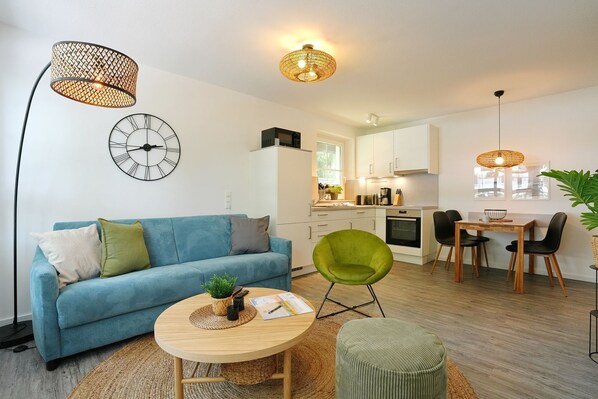 Una sala de estar moderna con un sofá, una mesa de centro redonda, una silla verde y una zona de comedor con una mesa y sillas.
