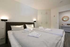 Habitación de hotel con dos camas, ropa de cama blanca, cabecera oscura, armario y un espejo en la pared.