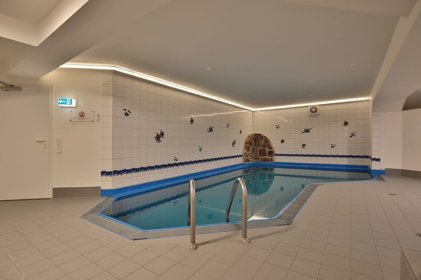 Ein Schwimmbecken mit einem Steingewölbe, gefliesten Wänden und einem blauen Rand.