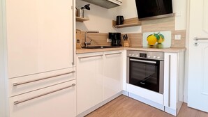 Una cocina compacta con horno Bosch, cafetera y tabla para cortar fruta.