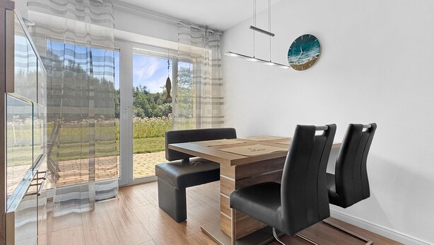 Un comedor moderno con una mesa de madera y sillas negras, ventanas amplias con cortinas y un reloj en la pared.