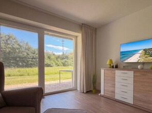 A modern room with a large sliding glass door leading to a balcony, a flat-screen TV on the wall, and a wooden cabinet with drawers. - 3005 - Sandy Near Grömitz - Apartment 3004 on Schoor in Grömitz (Grömitz)