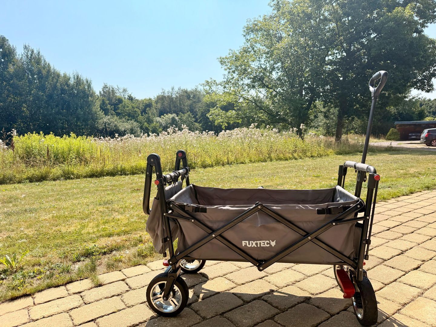 Een Fuxtec kinderwagen op een verhard pad, met gras en bomen op de achtergrond.