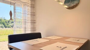 Un comedor con una mesa dispuesta para dos personas, una lámpara colgante y vistas al exterior con vegetación.