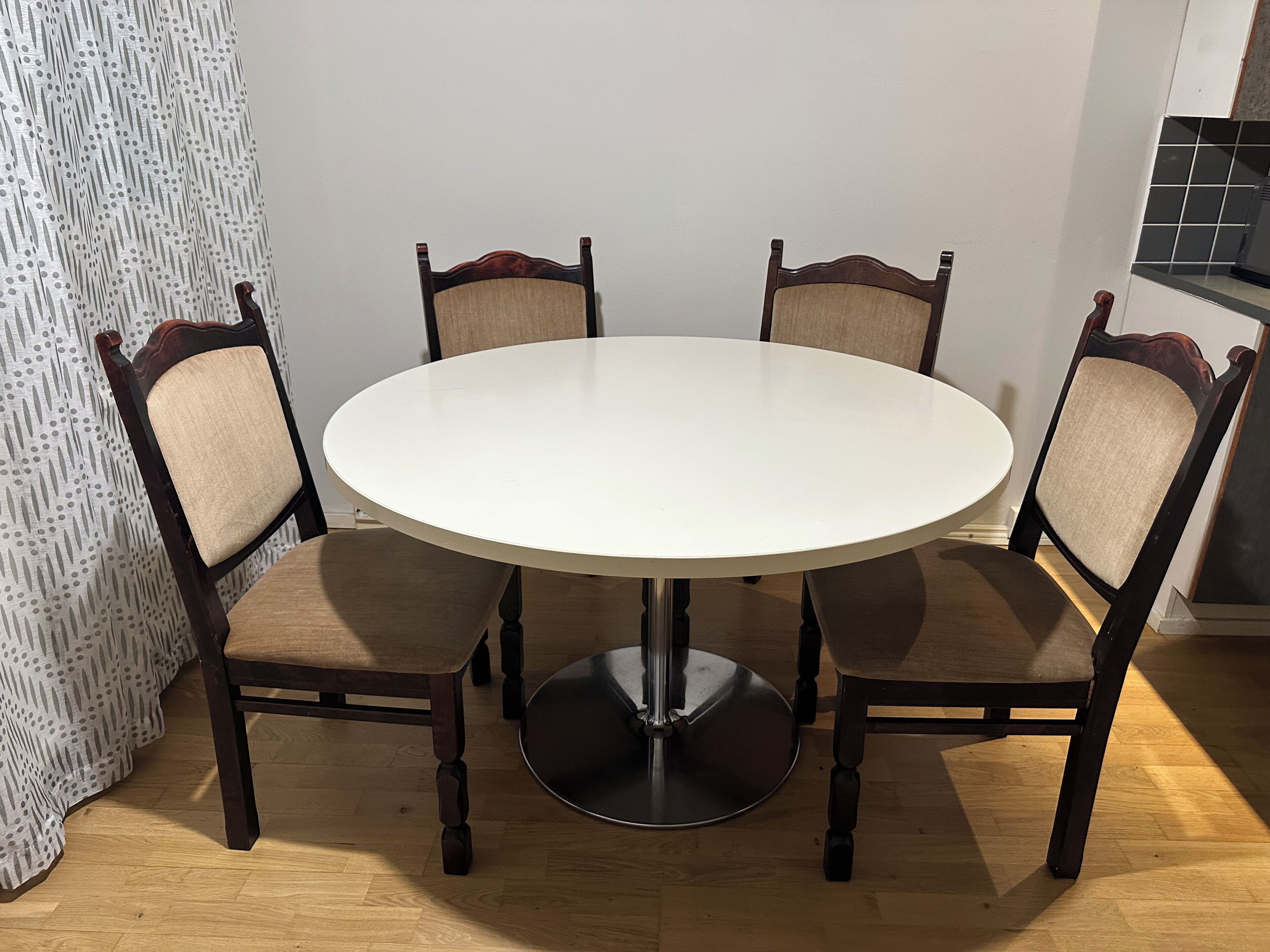 Une table de salle à manger ronde, avec quatre chaises, un pied en métal et un rideau à motifs en arrière-plan.