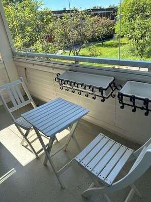A balcony with a table and chairs, a metal grill, and a view of greenery and buildings. - NOT LISTED (Helsinki)