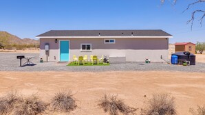 A single-story building with a blue door, a small porch with yellow chairs, and a blue utility shed in a desert setting. - Stylish Maricopa Cottage w/ Mtn Views & Grill! (Maricopa)