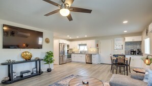 A spacious living area with a ceiling fan, a flat-screen TV, a dining table, and a kitchen with white cabinets and stainless steel appliances. - Stylish Maricopa Cottage w/ Mtn Views & Grill! (Maricopa)
