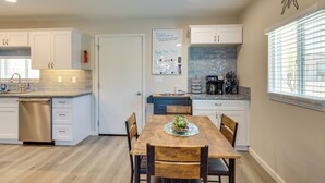 A modern kitchen with white cabinets, a wooden dining table, and a kitchen island. - Stylish Maricopa Cottage w/ Mtn Views & Grill! (Maricopa)