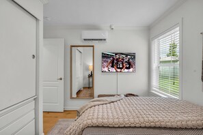 A bedroom with a bed, a TV, a mirror, and a window with blinds.