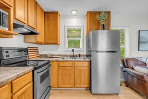 A modern kitchen with wooden cabinets, stainless steel appliances, a granite countertop, and a view of the outdoors through a window with blinds.