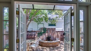 An open door to a patio with a brick fire pit, a chair, and a table. - Walk to Dtwn! Historic & Elegant Gem in Charlotte (Charlotte)