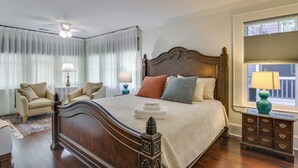 A bedroom with a large bed, a nightstand with a lamp, a chair, and a window with blinds. - Walk to Dtwn! Historic & Elegant Gem in Charlotte (Charlotte)
