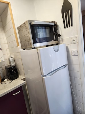 Eine Küche mit einer Mikrowelle auf einem weißen Kühlschrank, einer Bosch-Kaffeemaschine auf der Arbeitsplatte und einem an der Wand hängenden Pfannenwender.