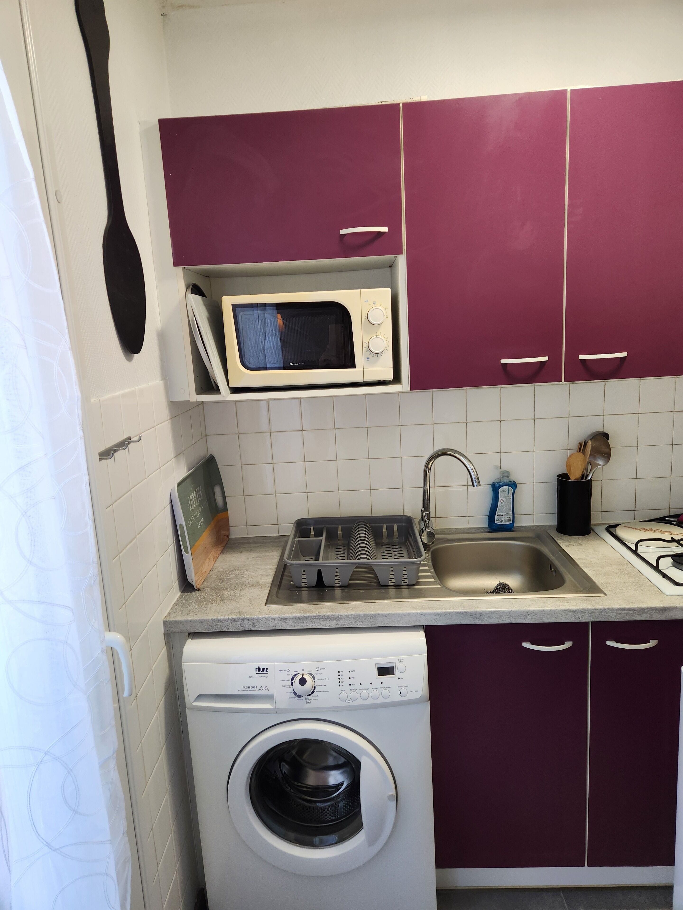 A compact kitchen with a microwave, sink, and washing machine.