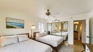 Ein Schlafzimmer mit zwei Betten, einem Deckenventilator, einem Gemälde und einem Spiegel.