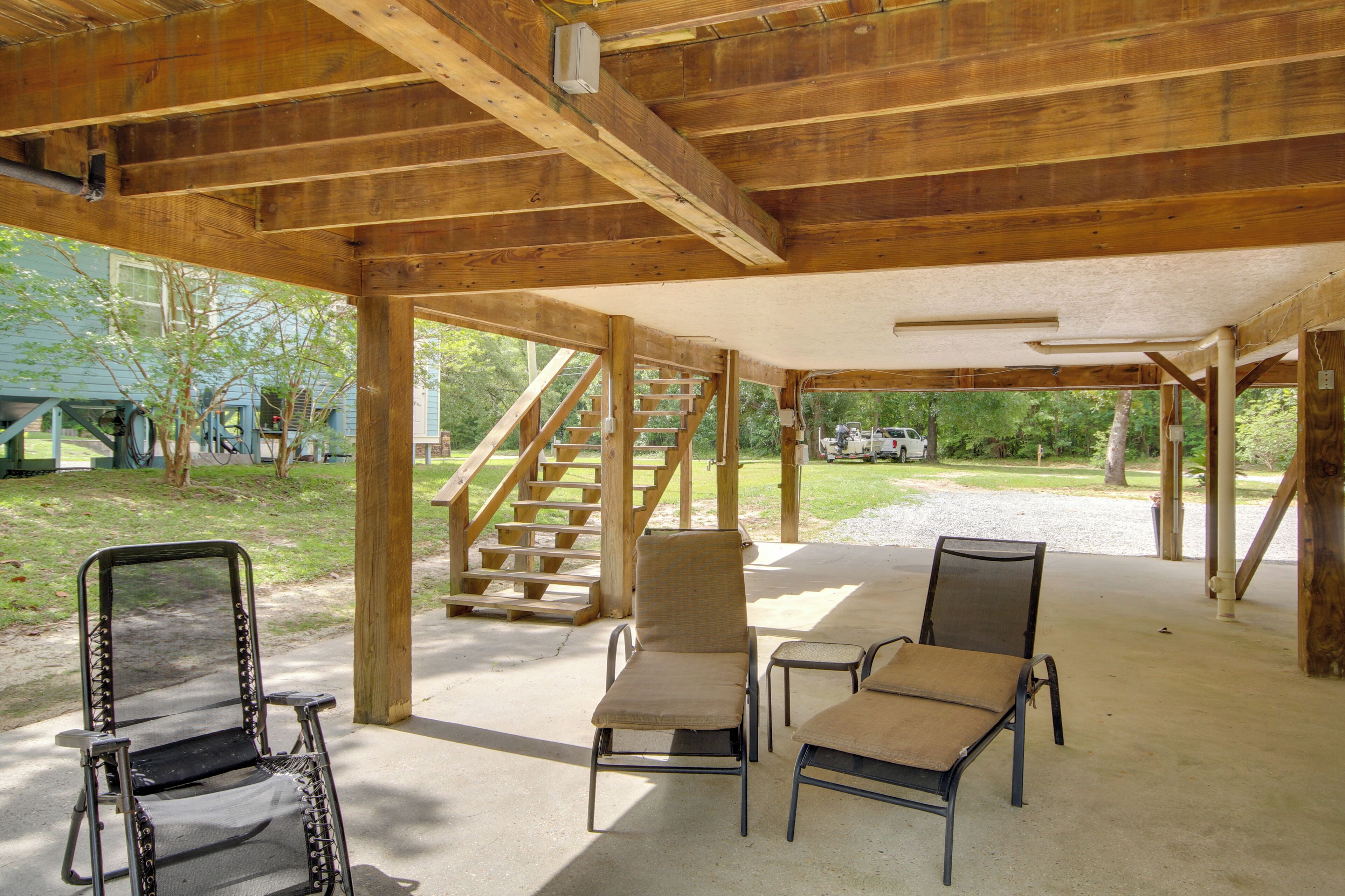 A covered outdoor area with wooden beams, concrete floor, and a set of stairs leading to a vehicle.