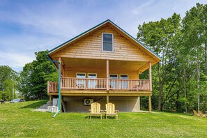 Une cabane en rondins à deux étages, dotée d’un balcon, d’un porche couvert et de deux fauteuils Adirondack dans le jardin.