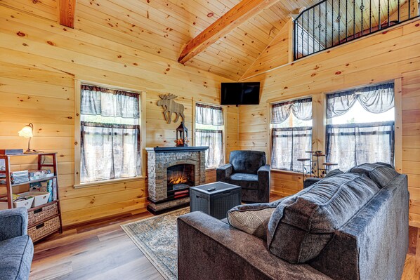 L’intérieur d’une cabane en rondins, avec une cheminée, un canapé, un fauteuil et un téléviseur.