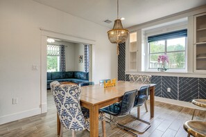 Ein Essbereich mit einem Holztisch, gemusterten Stühlen, einer Chandelierleuchtre und Blick ins Freie.