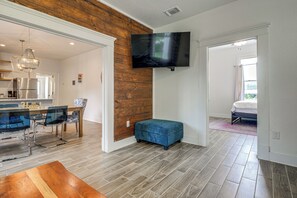 Ein modernes Wohnzimmer mit Fernseher, Holzvertäfelung, einer Essecke mit Stühlen und einer Küche im Hintergrund.