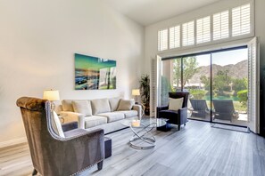 Ein geräumiges Wohnzimmer mit einer Couch, Sesseln, einem Glastisch und einem großen Fenster mit Blick ins Freie.