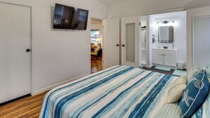 A bedroom with a bed, a TV mounted on the wall, and a door leading to a bathroom. - Newly Remodeled, Great Porches, and Dog Friendly (Port O'Connor)
