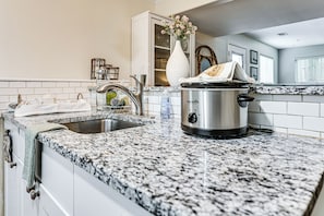 Una cocina con encimera de granito, una olla de acero inoxidable, un lavamanos y un armario blanco.