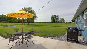 En terrasse med et bord, stole, en gul parasol og en grill.