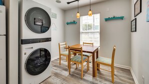 A compact kitchen with a built-in washer and dryer, wooden dining table, chairs, and pendant lighting. - Steps to Ocean! Family-Friendly Carolina Beach Gem (Carolina Beach)