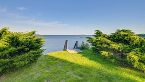 Une zone herbeuse avec une structure en bois menant à un plan d’eau, le tout entouré d’un feuillage verdoyant et dense.