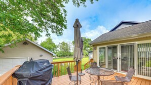 A wooden deck with a covered grill, outdoor table and chairs, and a large umbrella. - Fall Escape! Waterfront Chain O'Lakes Hideaway (Spring Grove)