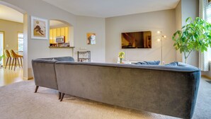 A living room with a grey sectional sofa, a flat-screen TV, a dining area with yellow chairs, and a large plant. - Spacious & Quiet Townhome In the Twin Cities (Roseville)