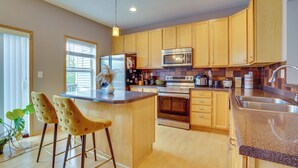 A modern kitchen with wooden cabinets, stainless steel appliances, and a central island with bar stools. - Spacious & Quiet Townhome In the Twin Cities (Roseville)