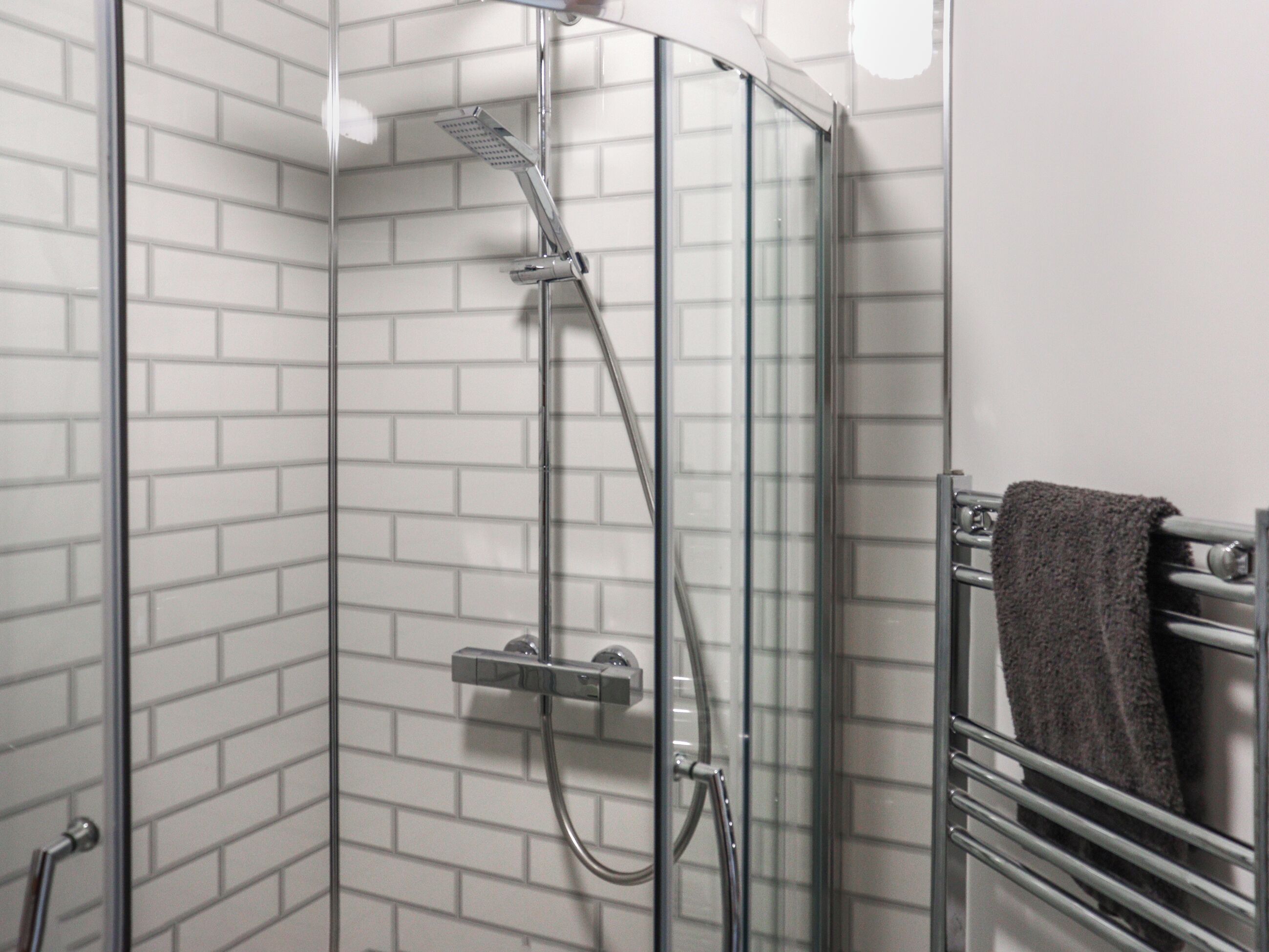 Een douche met glazen wand, een handdouche en een bedieningspaneel aan de muur.