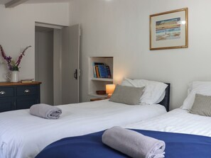 Ein Hotelzimmer mit zwei Betten, einem Bücherregal mit Büchern, einem gerahmten Bild an der Wand und einer Kommode mit Blumen in einer Vase.