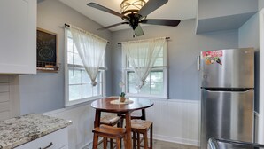 A kitchen with a round wooden table, two bar stools, a stainless steel refrigerator, and a ceiling fan.