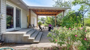 Eine überdachte Terrasse mit Treppe zu einem Haus, Gartenmöbel und ein Garten mit rosa Blumen.