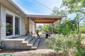 A covered patio with steps leading to a door, outdoor furniture, and a garden with pink flowers. - Explore Badlands Nat'l Park: Family Home w/ Patio (Kadoka)