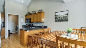 Una cocina con armarios de madera, un microondas y un comedor con mesa y sillas.