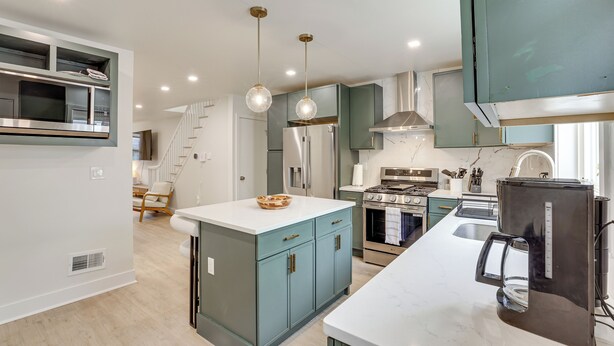 Une cuisine moderne avec des meubles de couleur turquoise, un îlot central, des appareils en acier inoxydable et des luminaires suspendus.