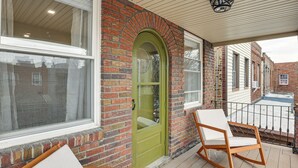 Un bâtiment en briques avec une porte verte, une chaise blanche et un balcon doté d’une balustrade.