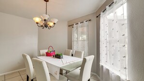 Uma sala de jantar com mesa, cadeiras, um lustre e uma janela com cortinas.