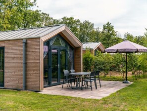 Ein modernes Gebäude mit Holzfassade, einem Glastür-Eingang und einer Terrasse mit Tisch und Stühlen.