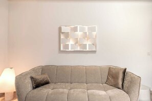 En sofastol i dæmpede farver med pude, vægmonteret lampe og gulvlampe.