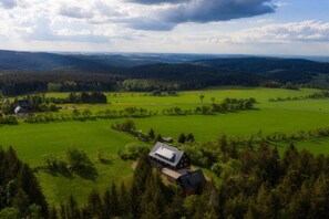 Ländliche Landschaft mit einem großen Haus, umgeben von grünen Feldern und Wäldern.