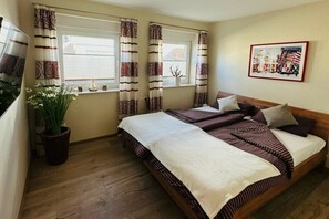 A bedroom with a bed, curtains, a potted plant, a framed picture, and a window. - Holiday apartment Crab Catcher (Borkum)
